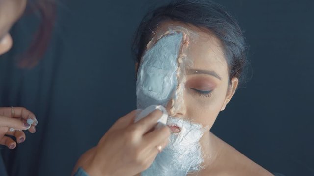 Close up of woman's face with zombie mask on one side of the face and make up artist making a mask 