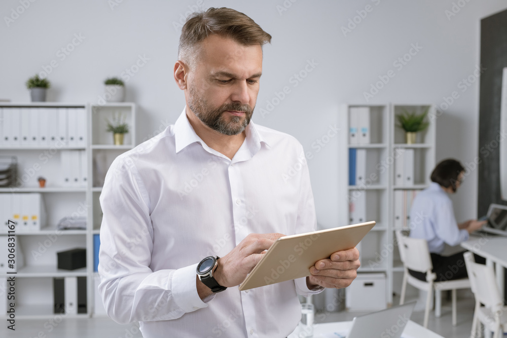 Poster serious employer in formalwear using touchpad to find information by workplace