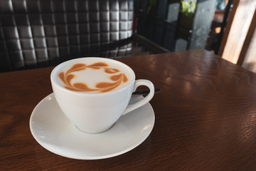 Cup of coffee latte on the wooden table in cafe. Close up, copy space