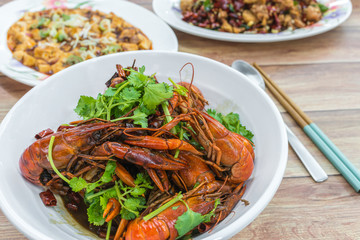 Chongqing Sichuan spicy dried chilli small lobsters, among other dishes in the background. Food photography at Chinese restaurant.
