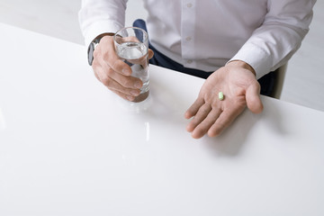 Elegant businessman in white shirt holding glass of water and painkiller