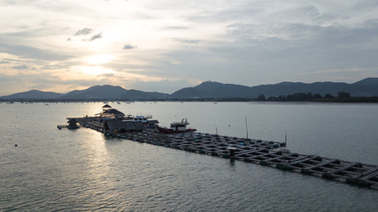 Obraz premium Thai fish farm on the center on the sea faraway from coastline, soft golden sunset over mountain on background