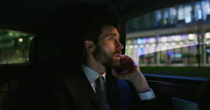 Slow motion of young handsome businessman driving a modern car in center of the city by night. Shot in 8K. Concept of business, success, traveling, luxury