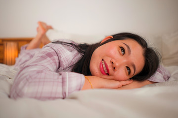Obraz na płótnie Canvas lifestyle portrait of young beautiful and sweet Asian Chinese woman in bed feeling happy and relaxed wearing cute pajamas enjoying lazy Sunday morning at home