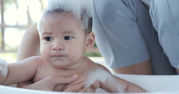 Mother washes the head of a small child. Newborn Baby Covered in Bubbles Close Up Playing in Bath.
