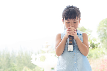 Cute asian little girl closed her eyes and folded her hand in prayer on a Holy Bible for faith concept