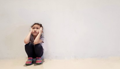 Sad little girl sitting against the wall in despair