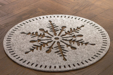 A light grey wool felt round dish mat in a shape of a flake of snow lying on a dark wooden table