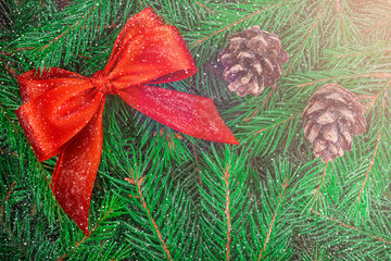 A beautiful large bow of red silk ribbon and two cones on the fluffy green branches of a Christmas tree, swirling snowflakes and yellow glow with copy space. Christmas, New Year greeting card concept.