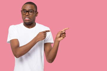 Nervous African American man in glasses pointing fingers at copy space