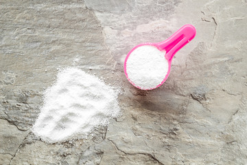 Washing powder in plastic spoon on grey background top view