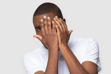 Scared unhappy African American man hiding behind hands