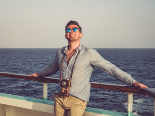 Fashionable man holding a vintage camera on the empty deck of a cruise liner against a background of sea waves. Side view, close-up. Concept of leisure and travel