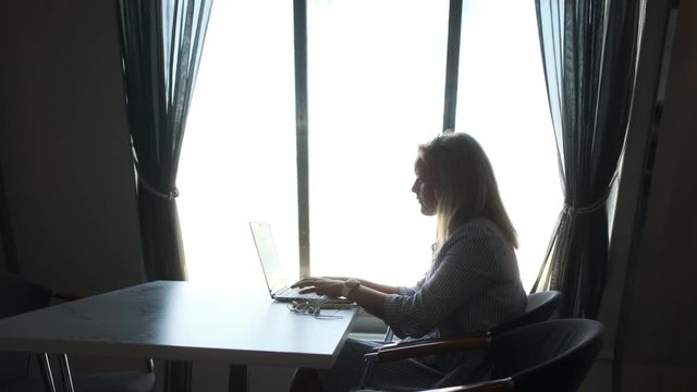Woman working / using a laptop in front of bright window v1