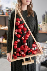 Alternative wooden christmas tree in womans hands . A handmade Christmas tree and red christmas balls.