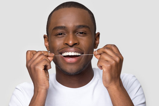 Happy African American man with healthy smile using dental floss