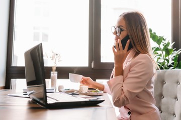 Business woman on the phone at office. Young business woman having phone call at the office. Smiling business woman. Pretty young business using smartphone at the loft office.