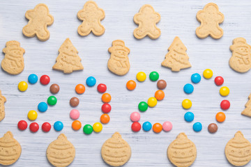 confectionery, on a light gray background, cookies in the form of a snowman, Santa Claus, Christmas toys and colorful dragees are laid out in the form of numbers, the next year