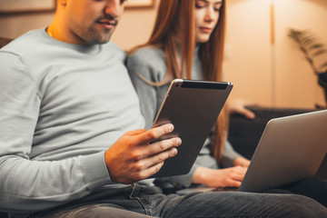 Close up hands of a man and woman sitting on a sofa and using a tablet and a laptop at home . Couple sitting on bed and using a tablet and laptop at home.