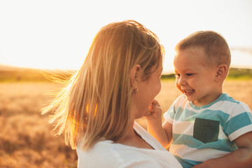 Close up portrait of lovely mother holding her little kid on arms and playing in a wheat field...
