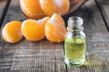 Essential oil with mandarin and slices of ripe yellow mandarin lie on a wooden table.
