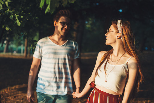 Beautiful red haired woman with freckles leading her boyfriend outdoor while dating looking at him smiling .