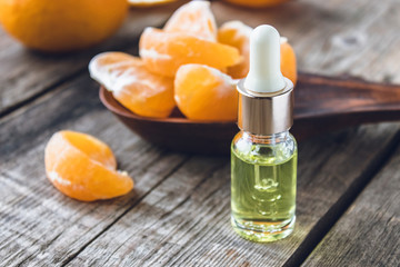 A glass bottle of essential oil with mandarin and slices of ripe mandarin are on the table.