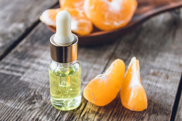Essential oil with mandarin and slices of ripe yellow mandarin lie on a wooden table.