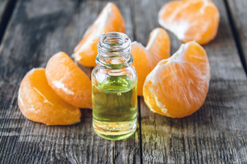 Essential oil with mandarin and slices of ripe yellow mandarin lie on a wooden table.