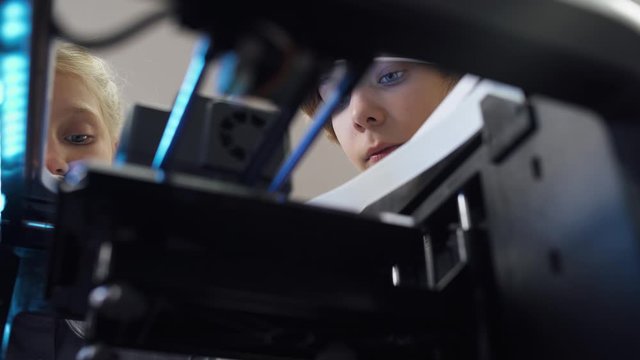 Education in the modern school, children learn modeling, boy and girl watching of process 3D printer prints.