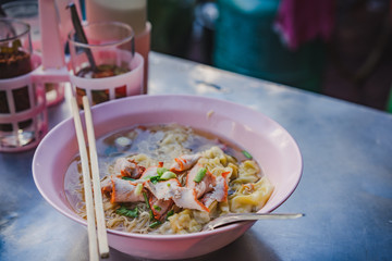 Egg noodle soup with red roasted pork and shrimp wonton in bowl at noodle shop street food.