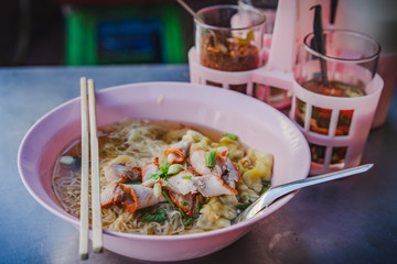 Egg noodle soup with red roasted pork and shrimp wonton in bowl at noodle shop street food.