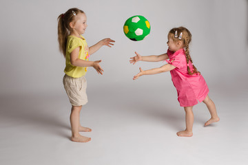 Side view of two cheerful kids throwing and catching ball on isolated background. Beautiful sisters...