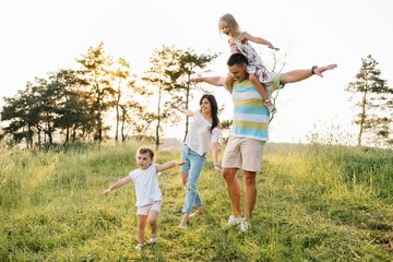 Color photo of smiling young parents and two children, rest and have fun in nature. Love, family and happy childhood lifestyle concept