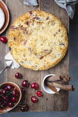 Homemade cherry crumble pie with fresh berries on rustic background, top view