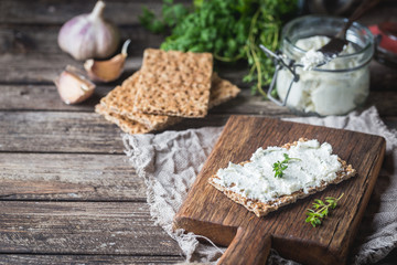 Obraz na płótnie Canvas Crispbread toast with homemade herb and garlic cottage cheese on wooden background