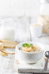 Bowl of oatmeal porridge with banana on white wooden rustic table, healthy breakfast, diet food.