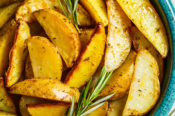 Baked potato wedges with rosemary in blue dish, top view. Healthy vegan food concept.