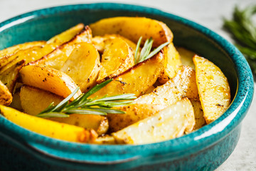 Baked potato wedges with rosemary in blue dish. Healthy vegan food concept.