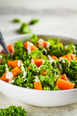 Kale and baked sweet potato salad with tahini dressing in white bowl. Healthy vegan food concept.