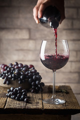 Pouring red wine into the glass against wooden background