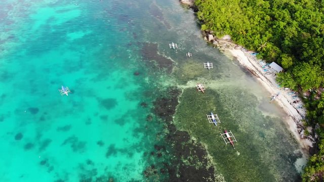 Aerial drone cinematic shot of small sandy beach with little boats and coral coast with turquoise clear water