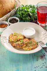 zucchini fritters with yogurt sauce and glass of red drink on blue wooden table
