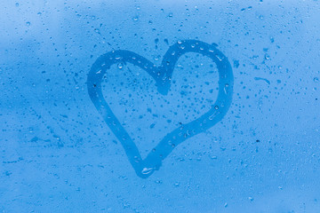 The child picture or figure of the heart on the blue evening or morning window glass with drops 