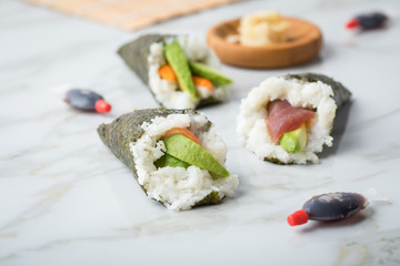 Lachs, Tunfisch und Surimi Avocado Temaki Sushi, eingelegter Ingwer mit Soja Soße Fische und Sushimatte auf Marmor Hintergrund