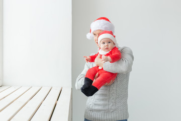 Fatherhood and holidays concept - Father with his baby boy wearing Santa hats celebrating Christmas