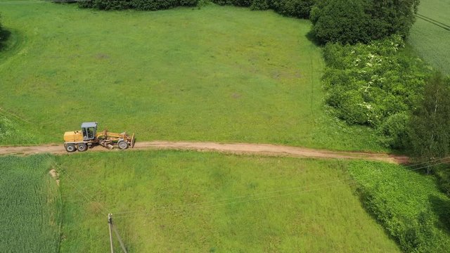 Road leveling motor grader on bad farmland road at work, aerial view