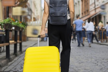 Fototapeta premium Luggage travel tourism concept, closeup of yellow suitcase in hand of walking woman