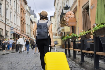 Traveling woman tourist in hat with backpack and suitcase walking