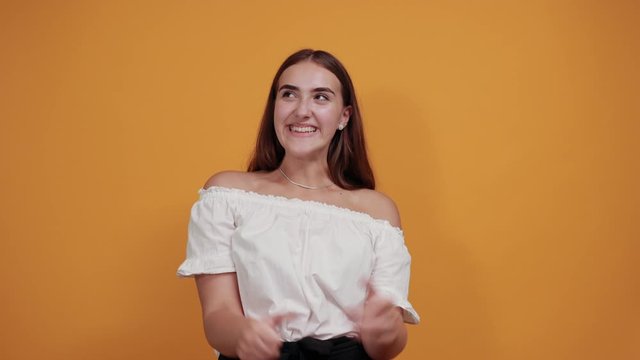 Happy young caucasian woman keeping fists up, smiling, looking pretty isolated on orange background in studio in casual white shirt. People sincere emotions, lifestyle concept.
